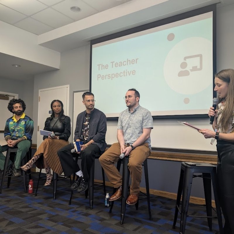 Dan seated with three other panelists on stools while a moderator speaks, in front of a screen titled The Teacher Perspective.